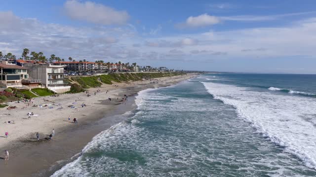 Low aerial view of the beach, the surf and palm trees in Carlsbad, with people walking.