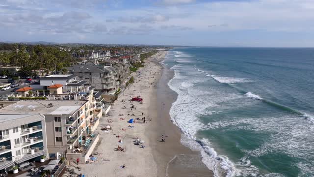 Low aerial view of the beach, the surf and palm trees in Carlsbad, with people walking.