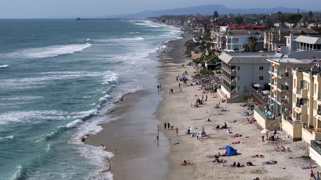 Low aerial view of the beach, the surf and the ocean in Carlsbad, with people walking.