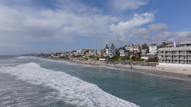 Low aerial view of the beach, the surf and the ocean in Carlsbad, with people walking.
