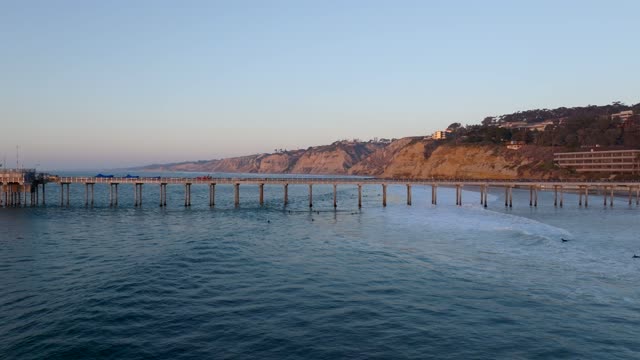 Low aerial view of the beach, the surf and the pier at La Jolla Shores, with surfers out.