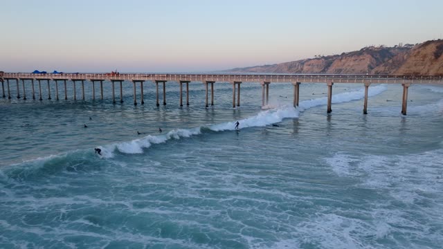 Low aerial view of the beach, the surf and the pier at La Jolla Shores, with surfers out.