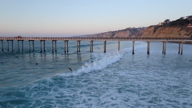 Low aerial view of the beach, the surf and the pier at La Jolla Shores, with surfers out.