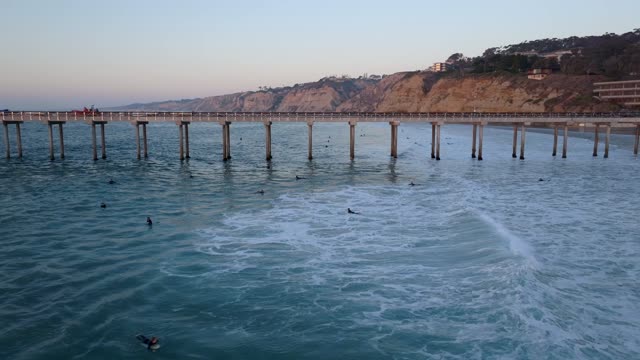 Low aerial view of the beach, the surf and the pier at La Jolla Shores, with surfers out.