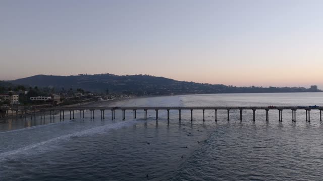 Low aerial view of the beach, the surf and the pier at La Jolla Shores, with surfers out.