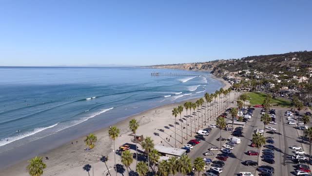 Low aerial view of the beach, the surf and the pier at La Jolla Shores, with surfers out.