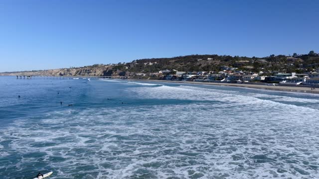 Low aerial view of the beach, the surf and the pier at La Jolla Shores, with surfers out.