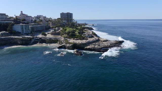 Aerial view of the cliffs, the surf and palm trees at La Jolla Cove, with people walking.
