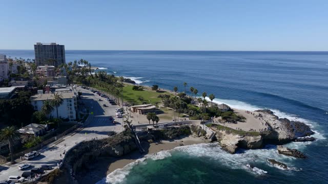 Aerial view of the cliffs, palm trees and the ocean at La Jolla Cove, with people walking.