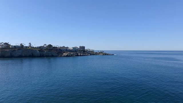 Low aerial view of the cliffs, palm trees and the ocean at La Jolla Cove.