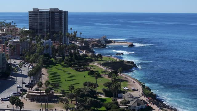 Aerial view of the cliffs, palm trees and the ocean at La Jolla Cove, with people walking.