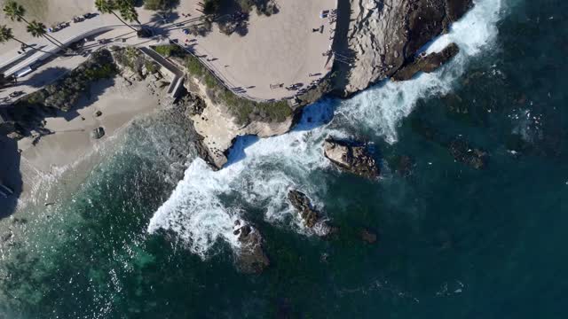 Aerial view of the cliffs, the surf and boats at La Jolla Cove, with people walking.