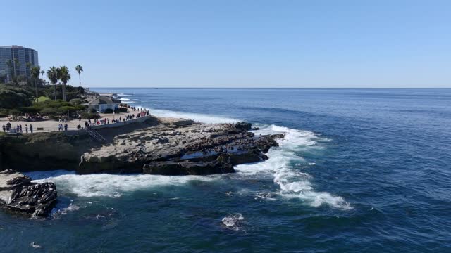 Low aerial view of the cliffs, the surf and wildlife at La Jolla Cove, with people walking.