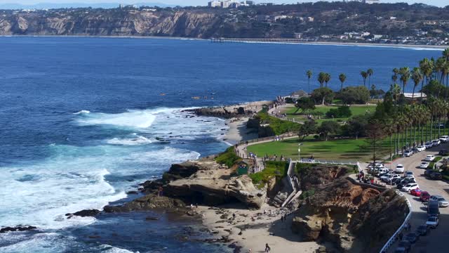 Aerial view of the cliffs, the surf and palm trees at La Jolla Cove, with people walking.