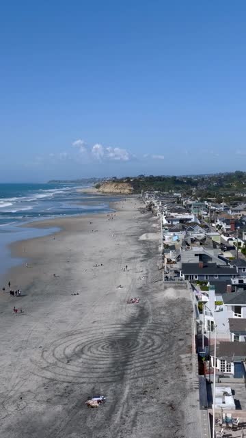 Aerial view of the beach, the surf and the ocean at Powerhouse Park, with people walking.