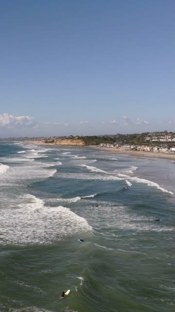Aerial view of the beach, the surf and the ocean at Powerhouse Park, with surfers out.