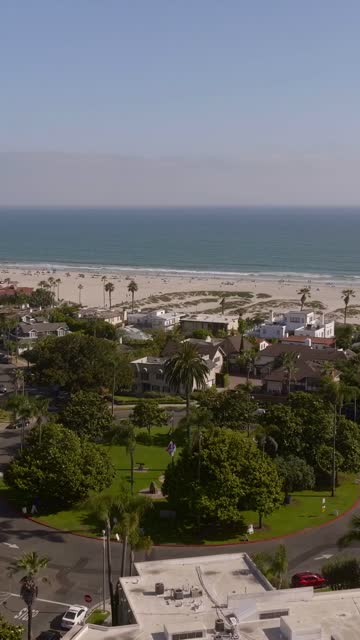 Aerial view of a residential street, palm trees and the ocean at Coronado Beach, with people walking.