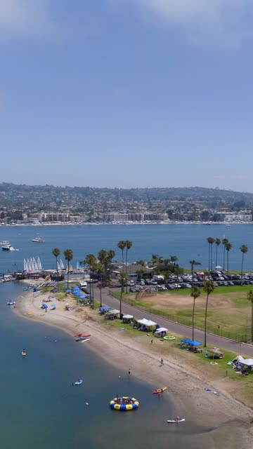 Aerial view of the beach, boats and palm trees in Mission Bay, with a crowd gathered.