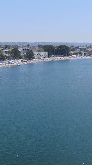 Aerial view of the beach, boats and the bay in Mission Bay, with a crowd gathered.
