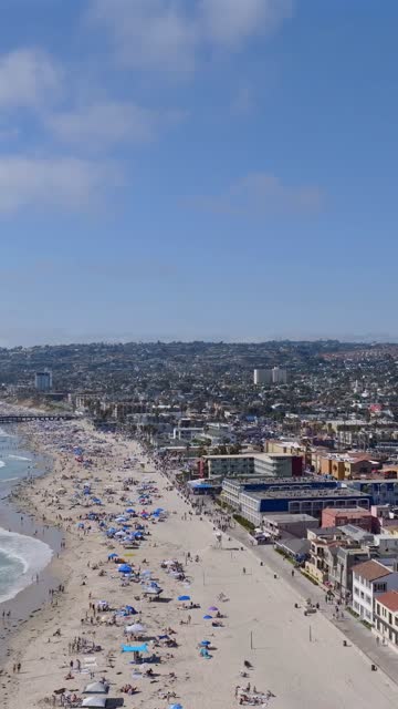 Aerial view of the beach, the ocean and homes in Mission Bay, with a crowd gathered.
