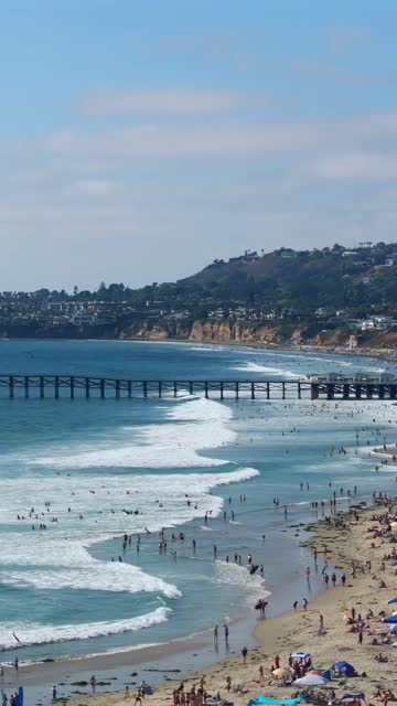 Aerial view of the beach, the surf and the pier in Mission Bay, with swimmers in the water.