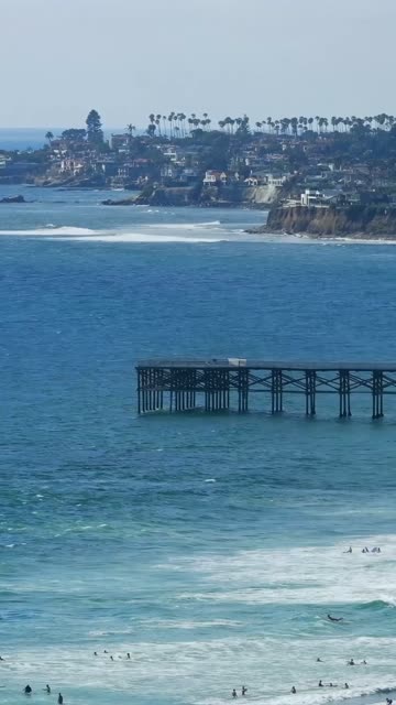 Aerial view of the beach, the surf and the pier in Mission Bay, with surfers out.