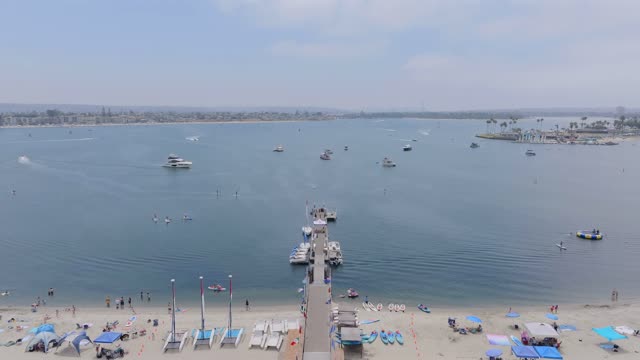 Aerial view of the beach, the pier and boats in Mission Bay, with a crowd gathered.