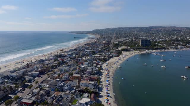 Aerial view of the beach, the pier and boats in Mission Bay, with a crowd gathered.