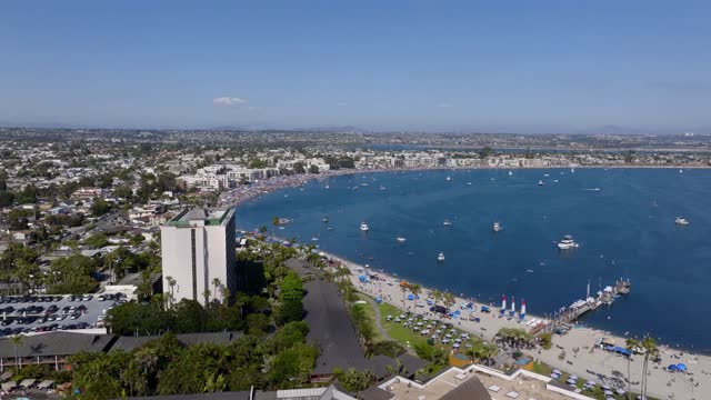 Aerial view of the beach, boats and palm trees in Mission Bay, with a crowd gathered.
