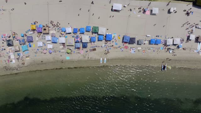 Aerial view of the beach, the bay and open country in Mission Bay, with a crowd gathered.