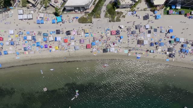 Aerial view of the beach, boats and the bay in Mission Bay, with a crowd gathered.