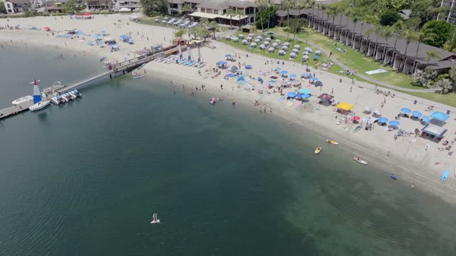 Aerial view of the beach, the pier and boats in Mission Bay, with a crowd gathered.