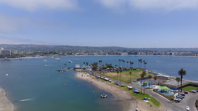 Aerial view of the beach, boats and palm trees in Mission Bay, with a crowd gathered.