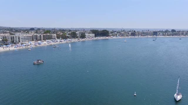 Aerial view of the beach, boats and palm trees in Mission Bay, with a crowd gathered.
