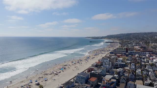 Aerial view of the beach, the surf and the pier in Mission Bay, with a crowd gathered.