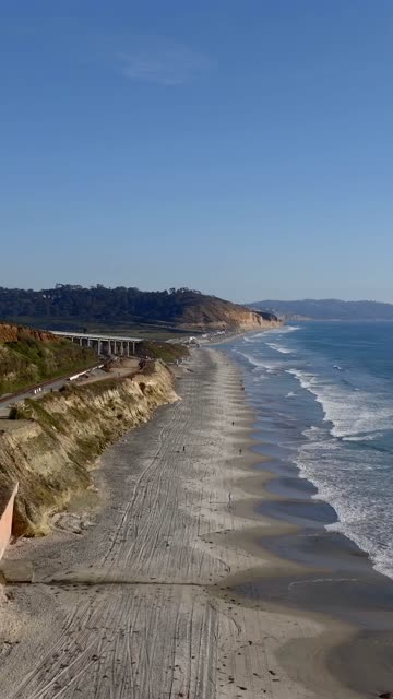 Aerial view of the cliffs, the surf and the bridge at Torrey Pines, with people walking.