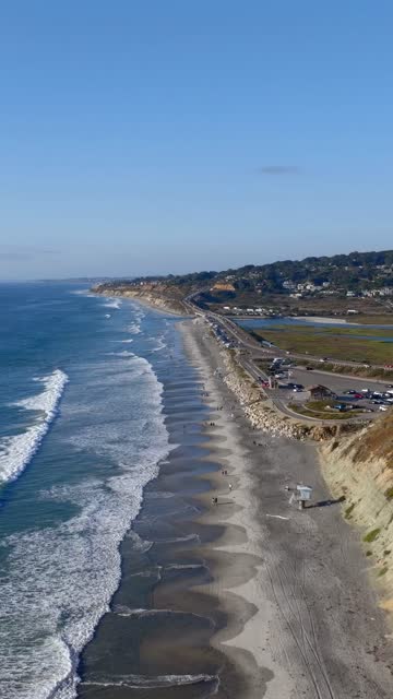 Aerial view of the beach, the surf and the ocean at Torrey Pines, with people walking.