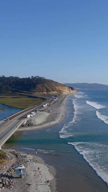 Aerial view of the beach, the surf and the bridge at Torrey Pines, with people walking.