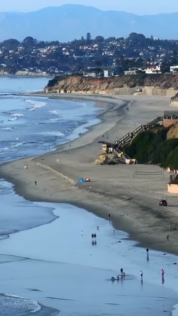 Aerial view of the beach, the ocean and homes in Del Mar, with people walking.