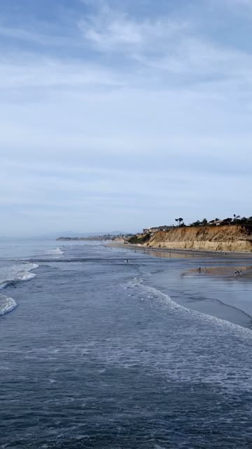 Aerial view of the beach, the surf and the ocean in Del Mar, with people walking.
