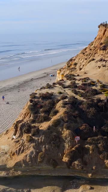 Aerial view of the cliffs, the ocean and the beach in Del Mar, with people walking.