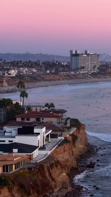 Aerial view of the cliffs, palm trees and the ocean at Bird Rock, with surfers out.