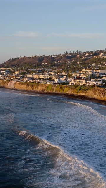 Aerial view of the cliffs, the surf and the ocean at Bird Rock, with surfers out.