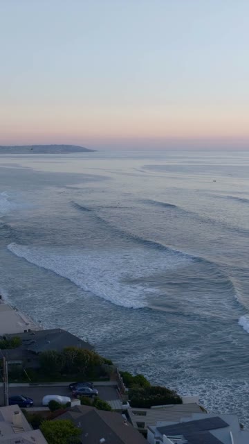Aerial view of the cliffs, the surf and the ocean at Bird Rock, with surfers out.