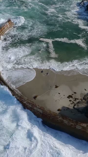 Aerial view of the beach, the surf and the ocean at Village of La Jolla, with people walking.