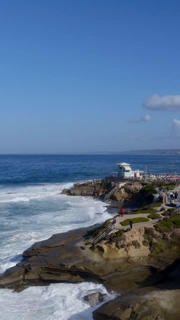 Low aerial view of the cliffs, the surf and the ocean at Village of La Jolla, with people walking.