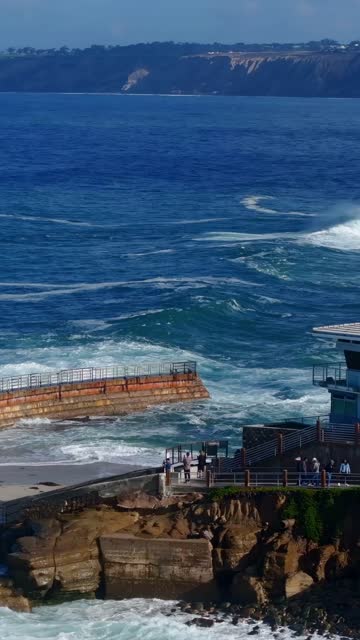 Aerial view of the cliffs, the surf and the ocean at Village of La Jolla, with people walking.