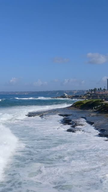 Low aerial view of the cliffs, the surf and the ocean at Village of La Jolla.