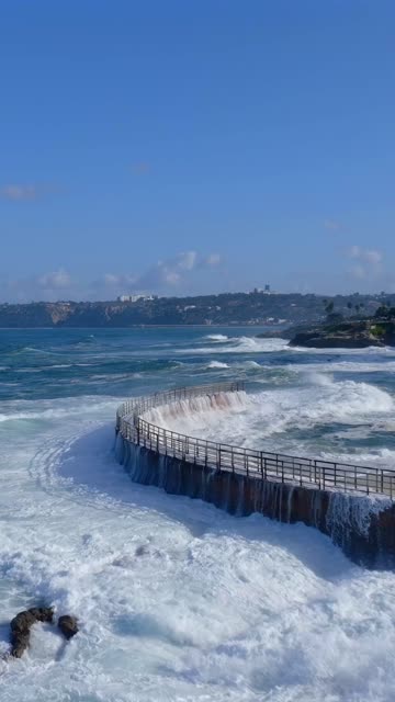 Low aerial view of the cliffs, the surf and palm trees at Village of La Jolla.