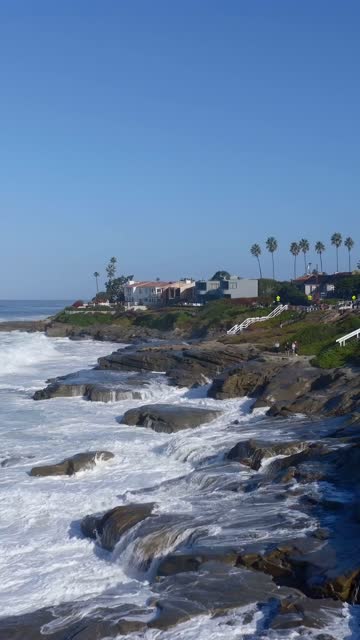 Low aerial view of the cliffs, the surf and palm trees at Beach Barber Tract, with people walking.